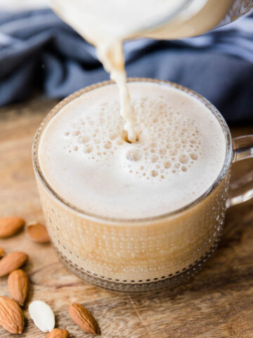 Homemade almond milk being poured into glass coffee mug.