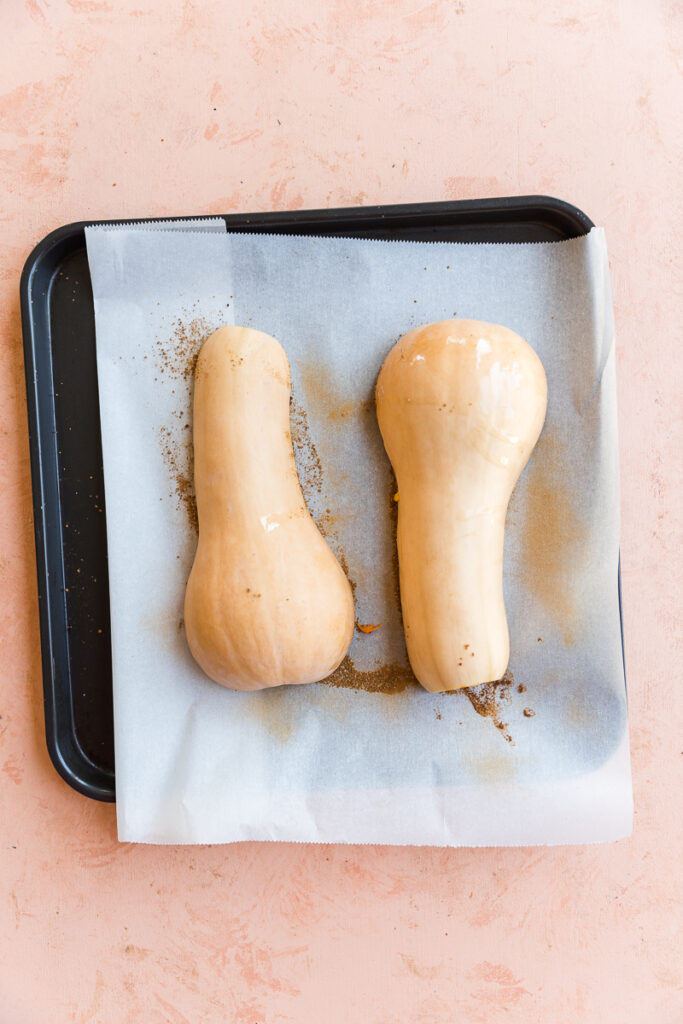 Butternut squash halves face down on parchment paper.