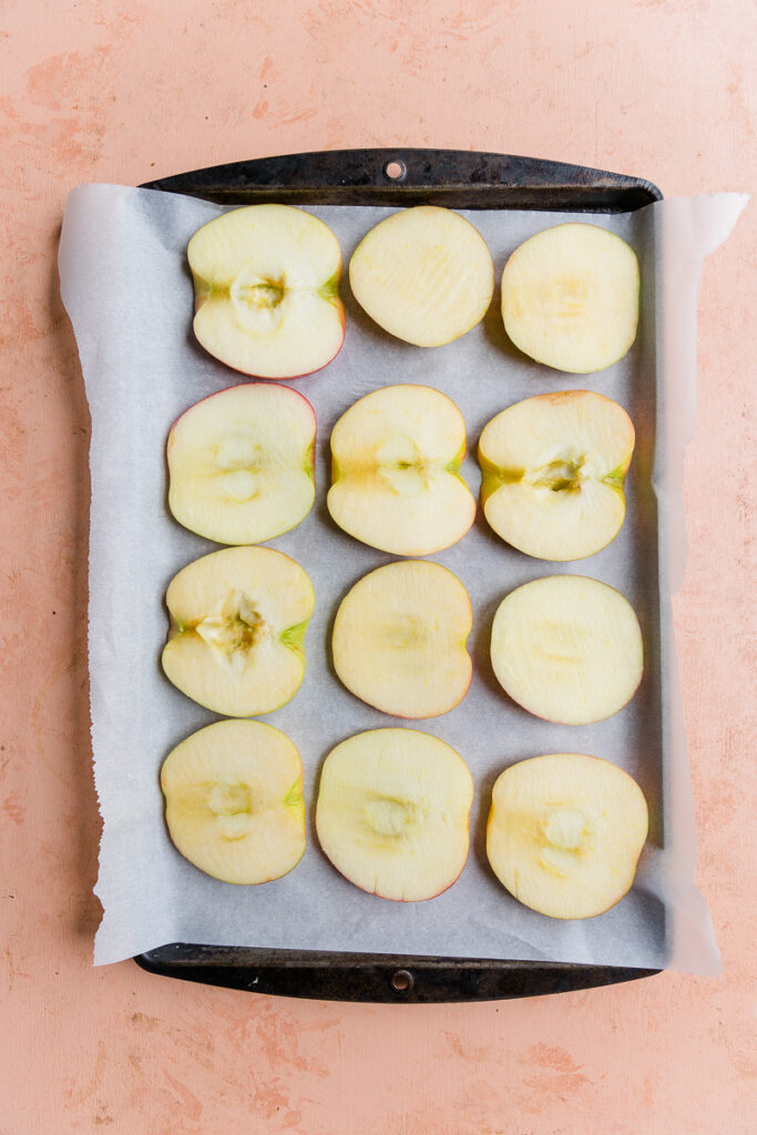 Sliced apples on a parchment paper lined baking sheet.