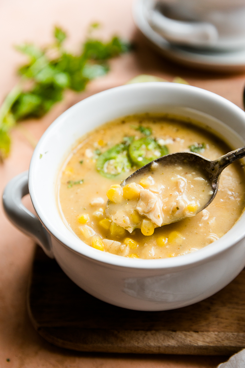 Spoon scooping out Mexican street corn soup from a white ceramic bowl.