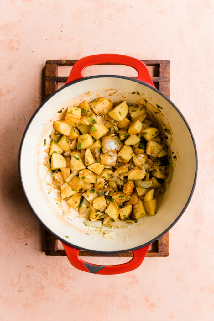 Vegetables and spices cooking at the bottom of a pot.