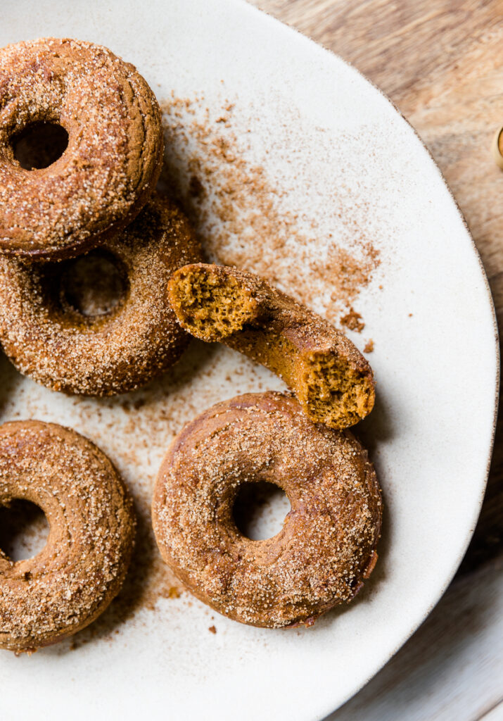 Pumpkin donuts on a plate tossed in cinnamon and sugar.