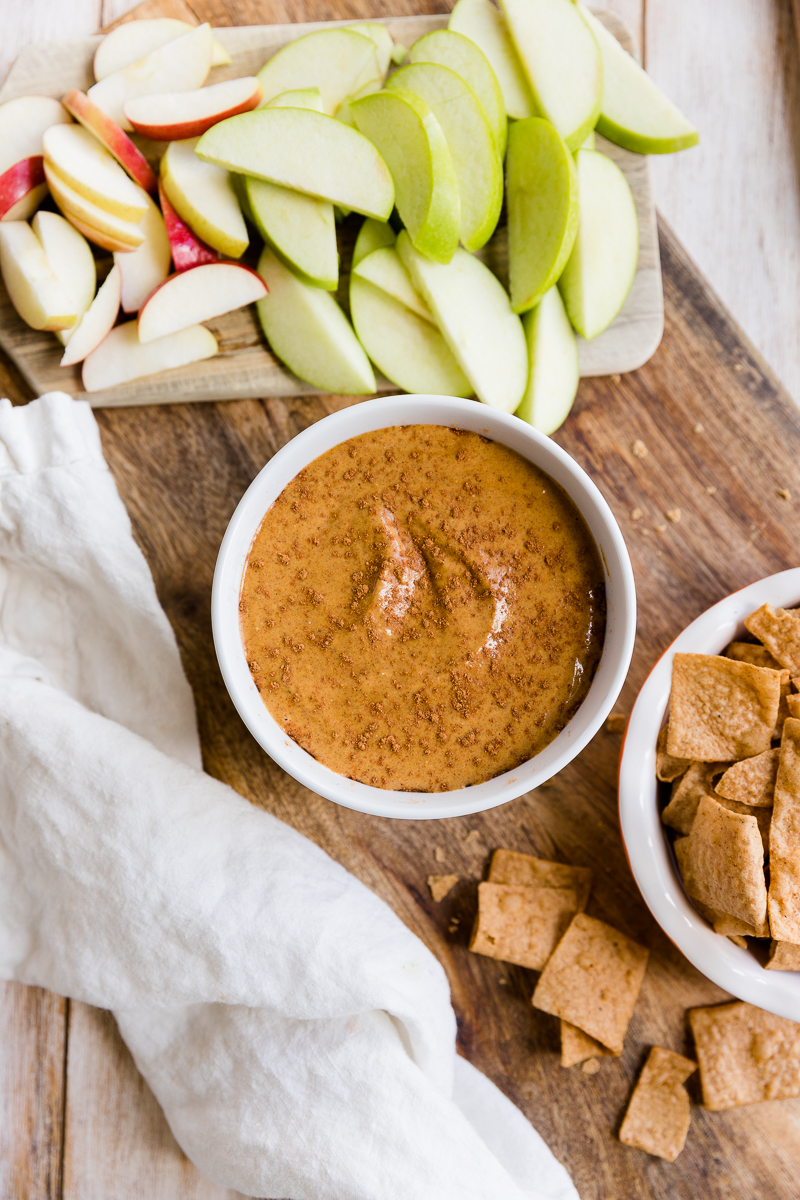 Pumpkin dip in a bowl surrounded by apple slices and churro chips.