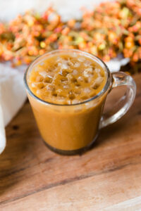 Pumpkin spice iced latte with small ice cubes in glass mug.