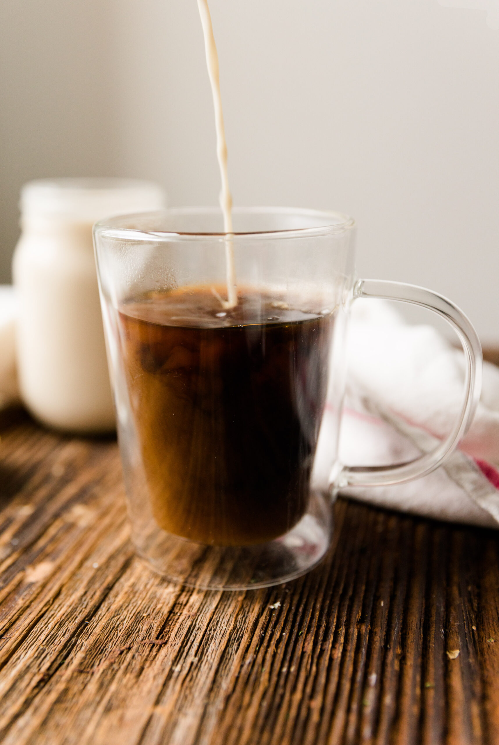 Vanilla creamer being poured into hot coffee in a glass mug.