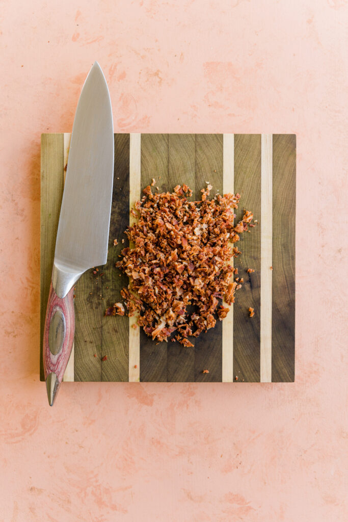 Cooked bacon finely chopped on a cutting board.