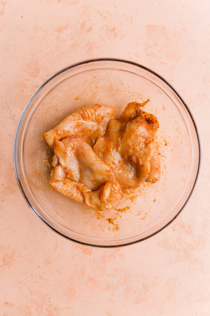 Chicken breast marinating in a glass mixing bowl.
