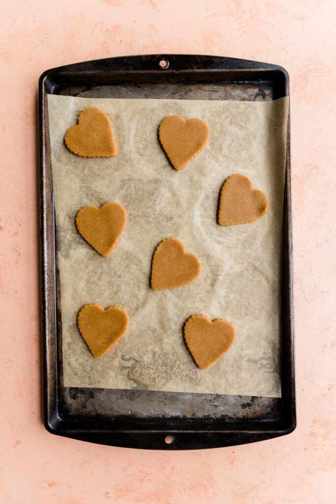 Heart sugar cookies on parchment paper lined baking sheet.