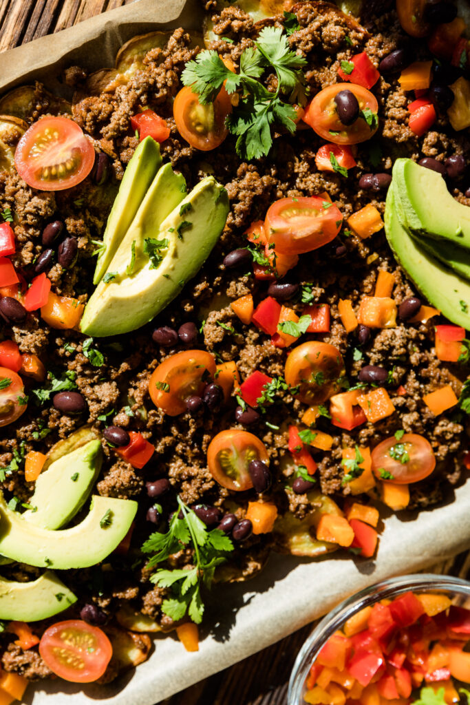 Potato nachos with ground beef, avocado, grape tomatoes, black beans, and bell peppers on top.