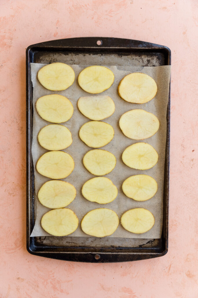 Potato discs spaced out on a parchment paper lined baking sheet.