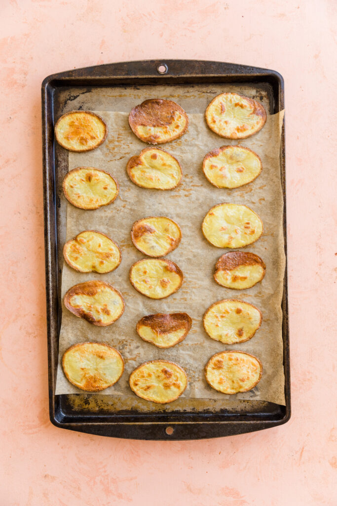 Crispy potato discs on a parchment paper lined baking sheet.