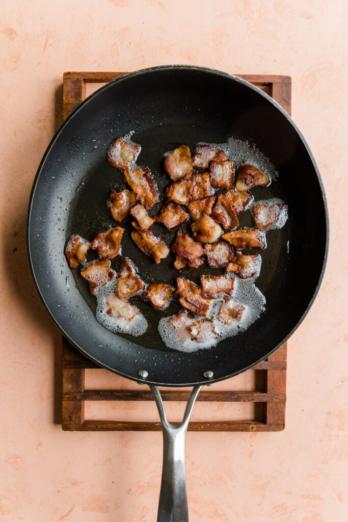 Crispy bacon cooking in a frying pan.