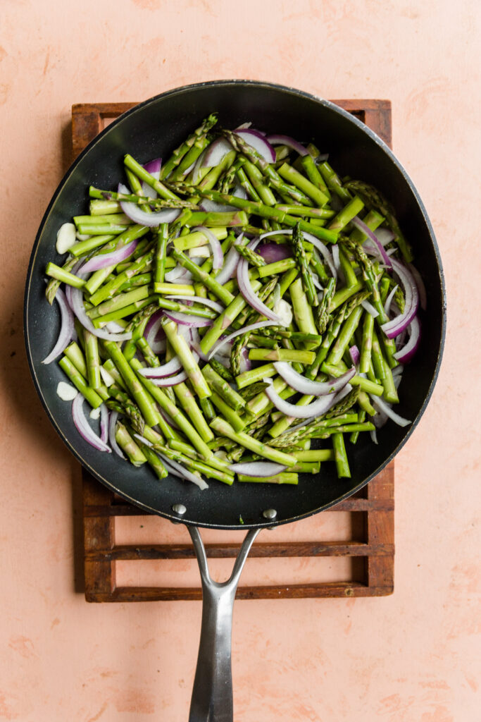 Asparagus, red onion, and garlic cooking in a frying pan.
