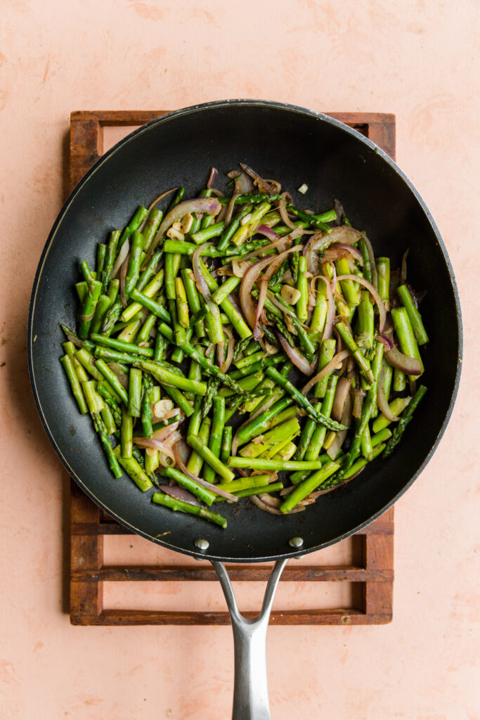 Cooked asparagus, red onion, and garlic in a frying pan.