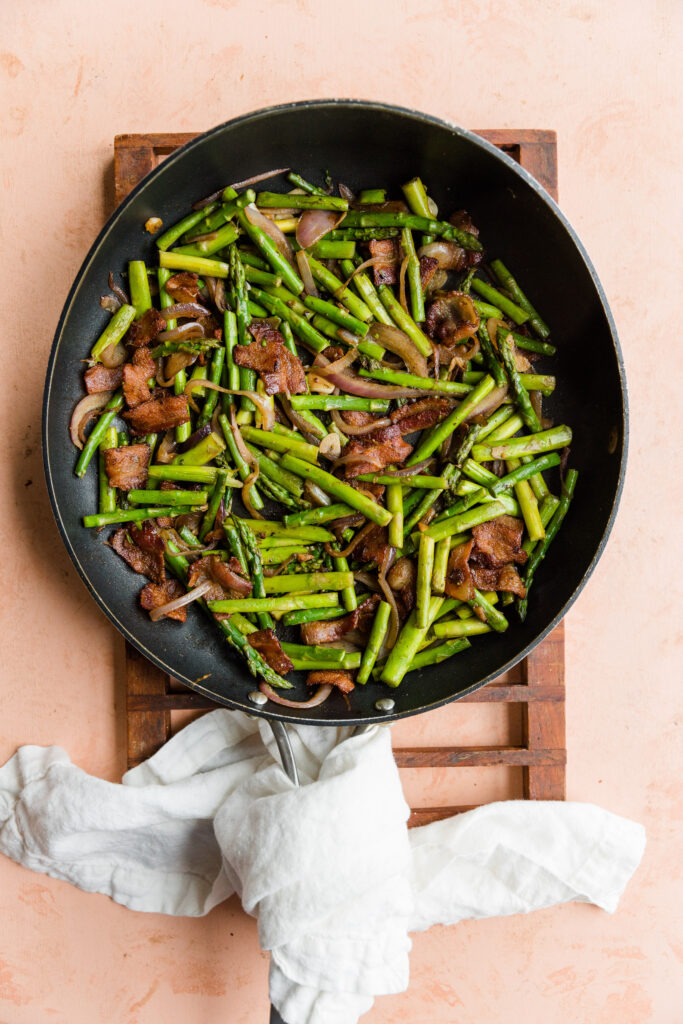 Bacon, asparagus, red onion, and garlic in large pan with towel wrapped around the handle.