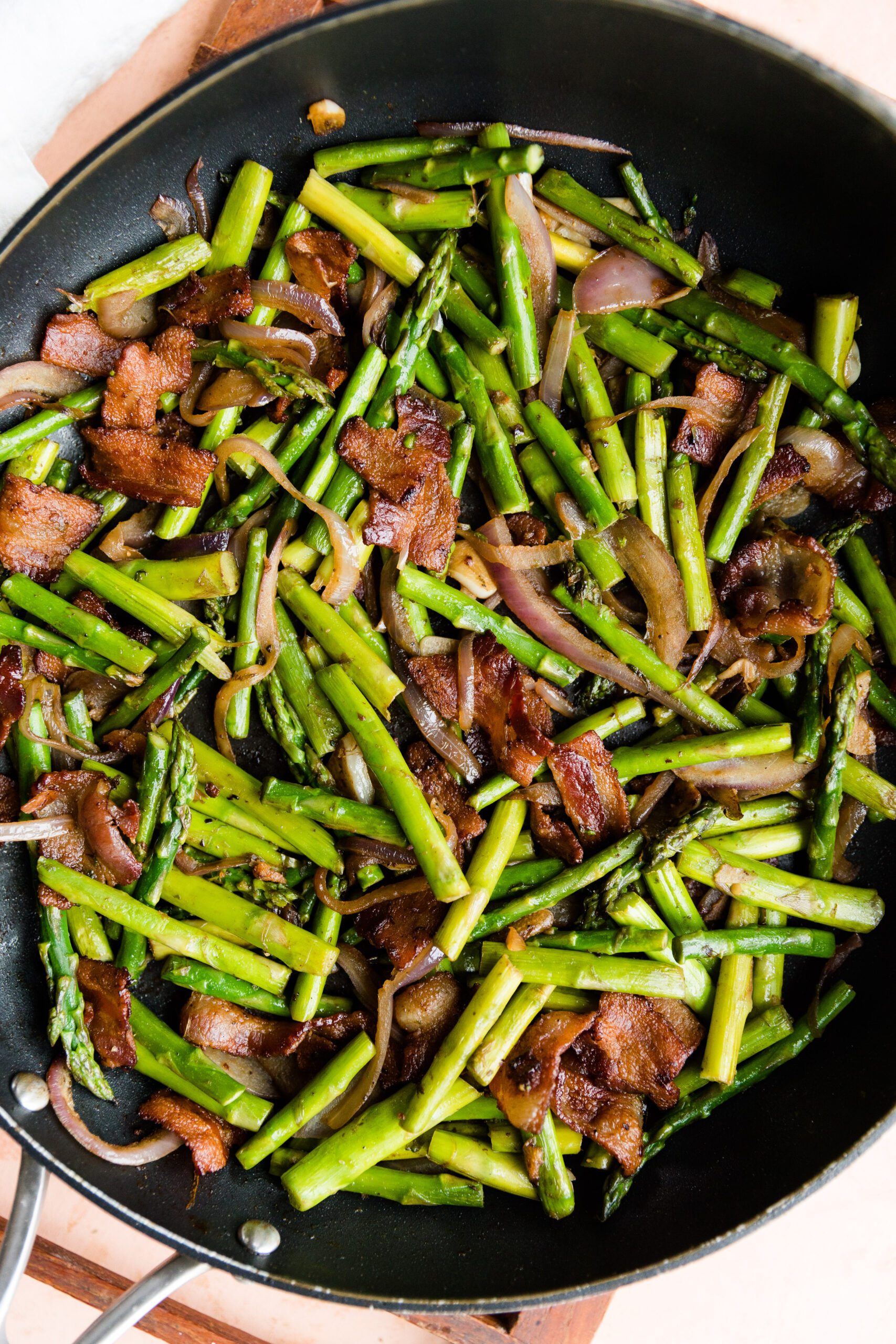 Close up picture of asparagus with bacon in large skillet.