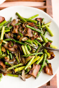 Sauteed asparagus with crispy bacon on a white ceramic plate.