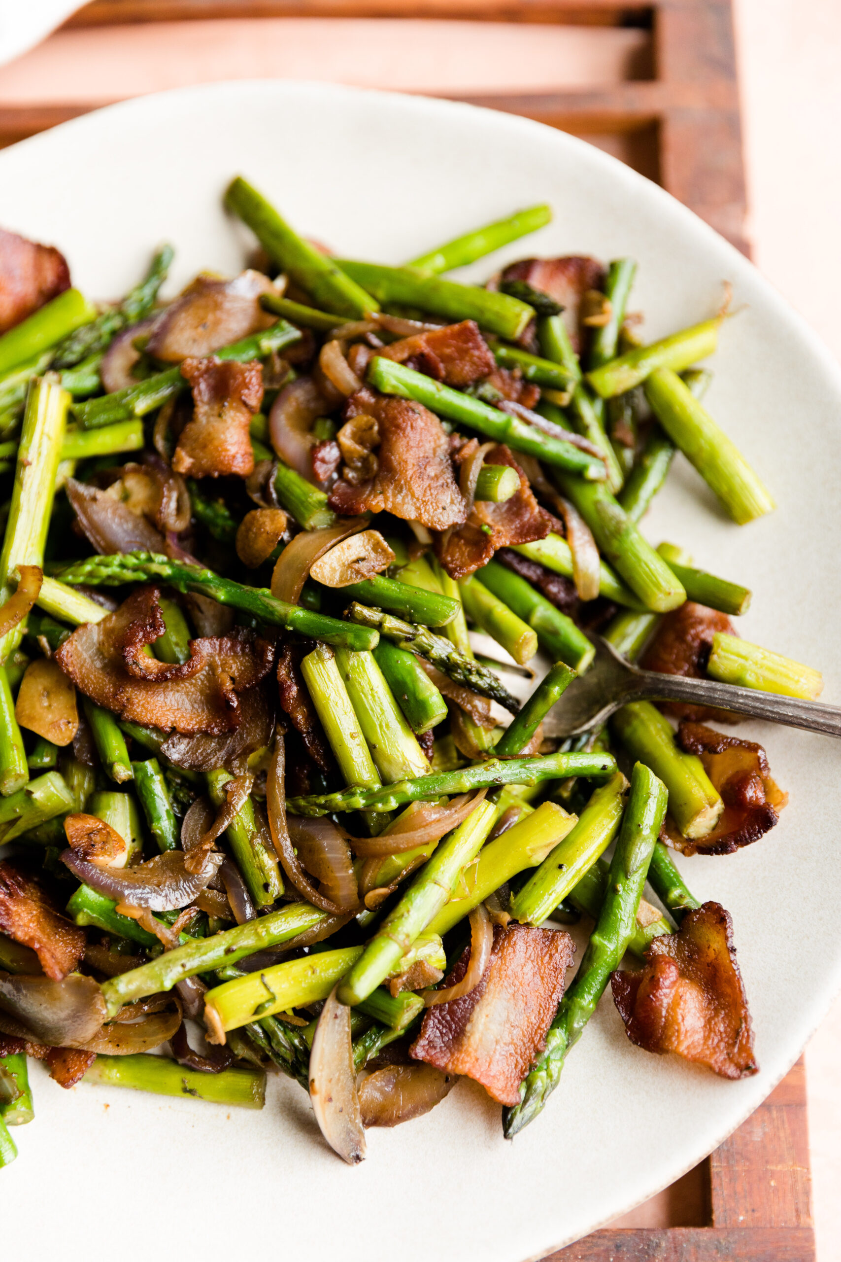Sauteed asparagus with crispy bacon on a white ceramic plate.
