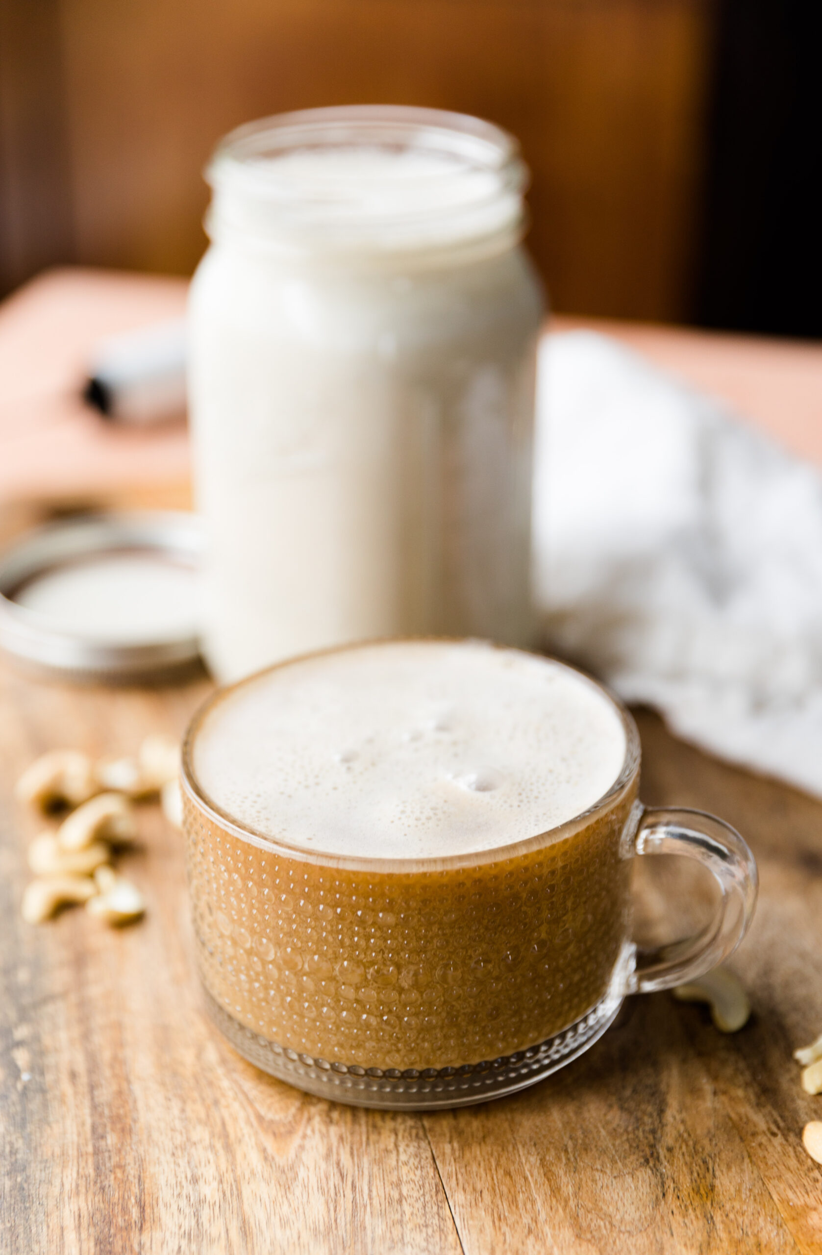 Large glass coffee cup filled with coffee and cashew creamer. Mason jar with cashew creamer in the background.