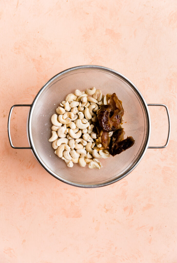 Cashews and dates in metal strainer.