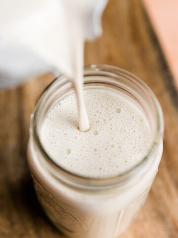 Pouring creamy cashew milk into a large glass mason jar.
