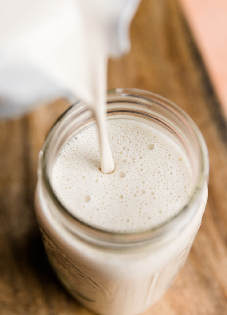 Pouring creamy cashew milk into a large glass mason jar.