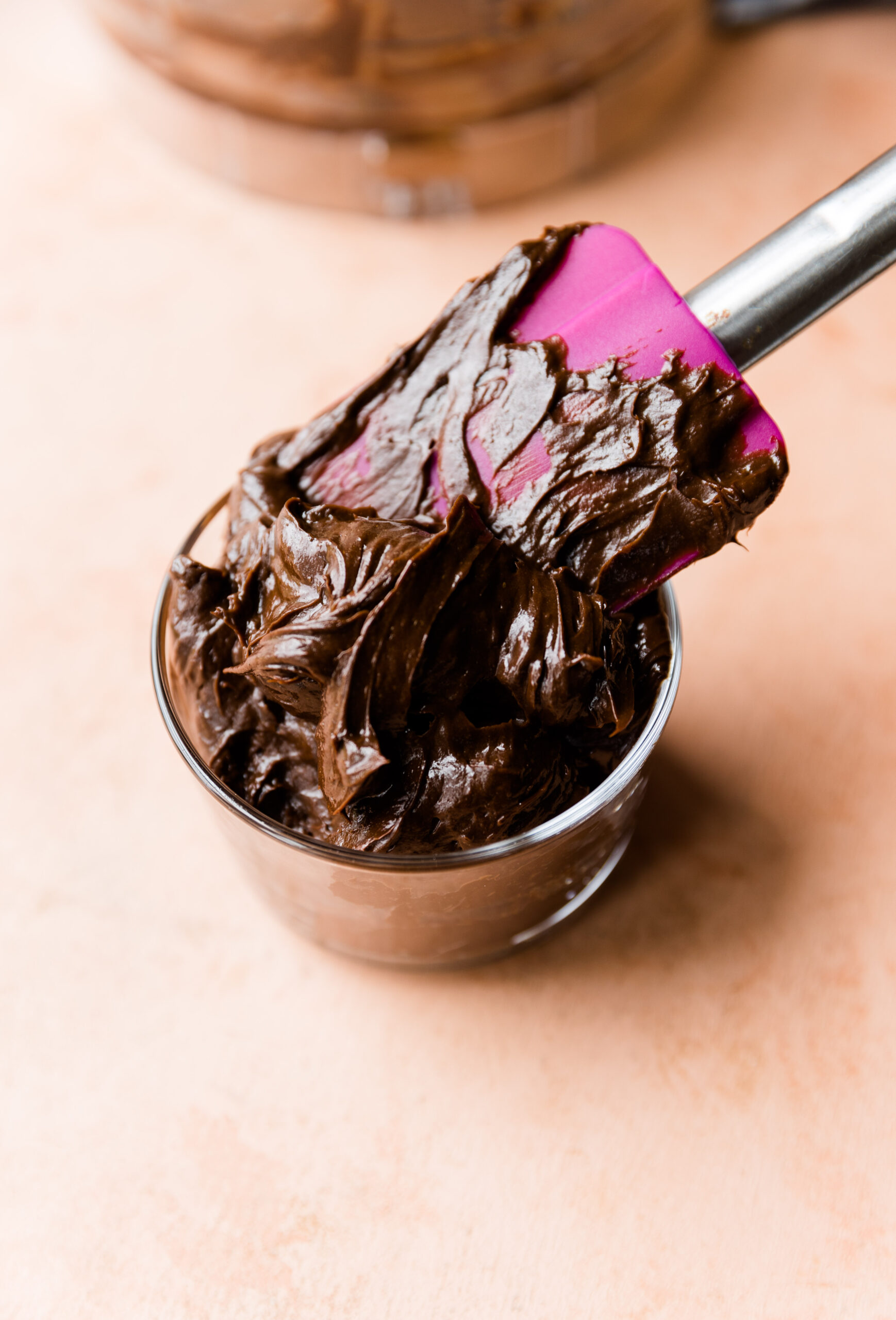 Chocolate avocado frosting in a small glass jar with a spatula.