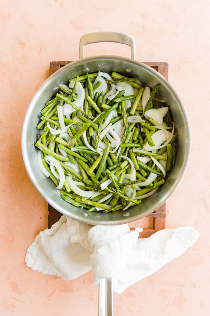 Uncooked onions, asparagus, and green beans in large pan.