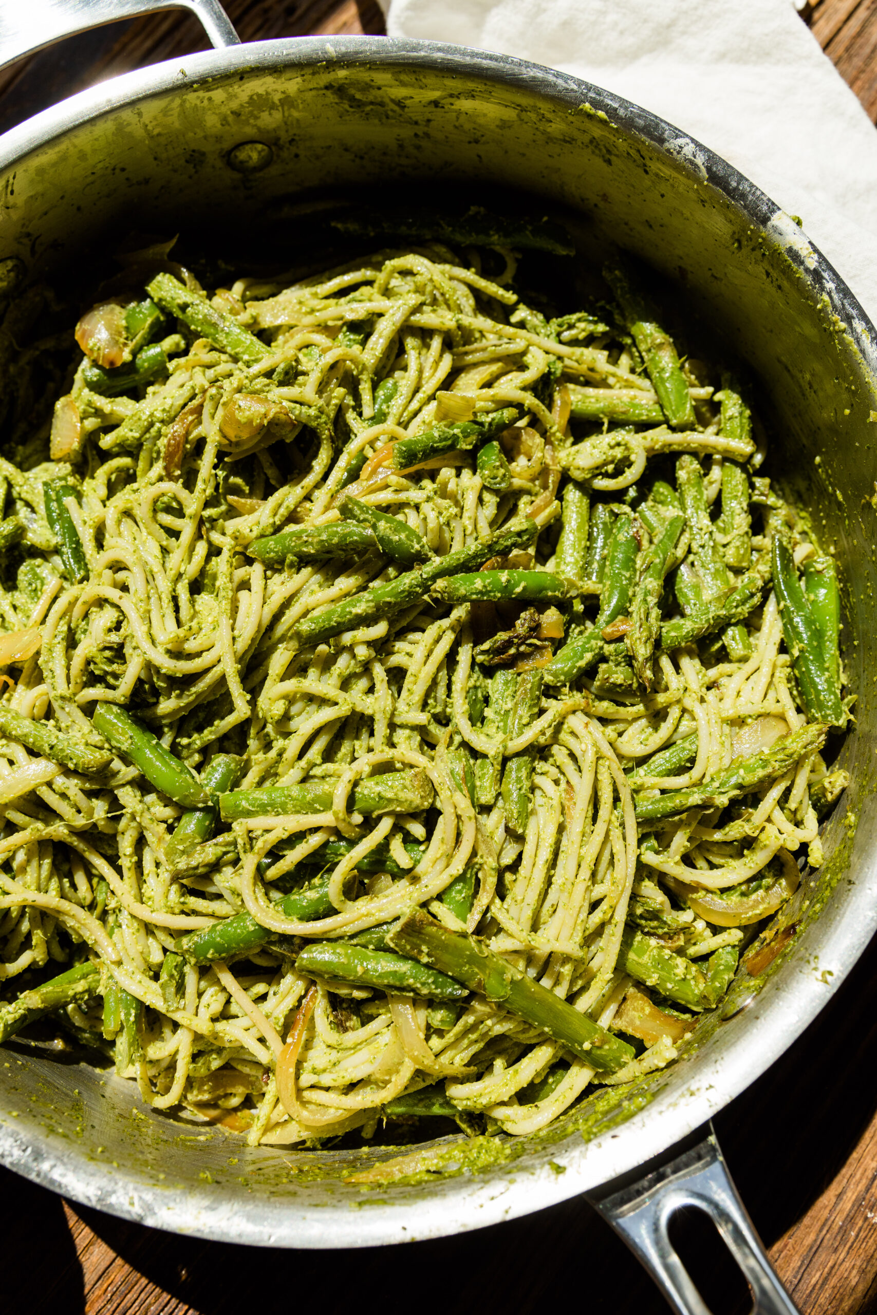 Close up picture of pesto pasta with asparagus, onions, and green beans in a pan.