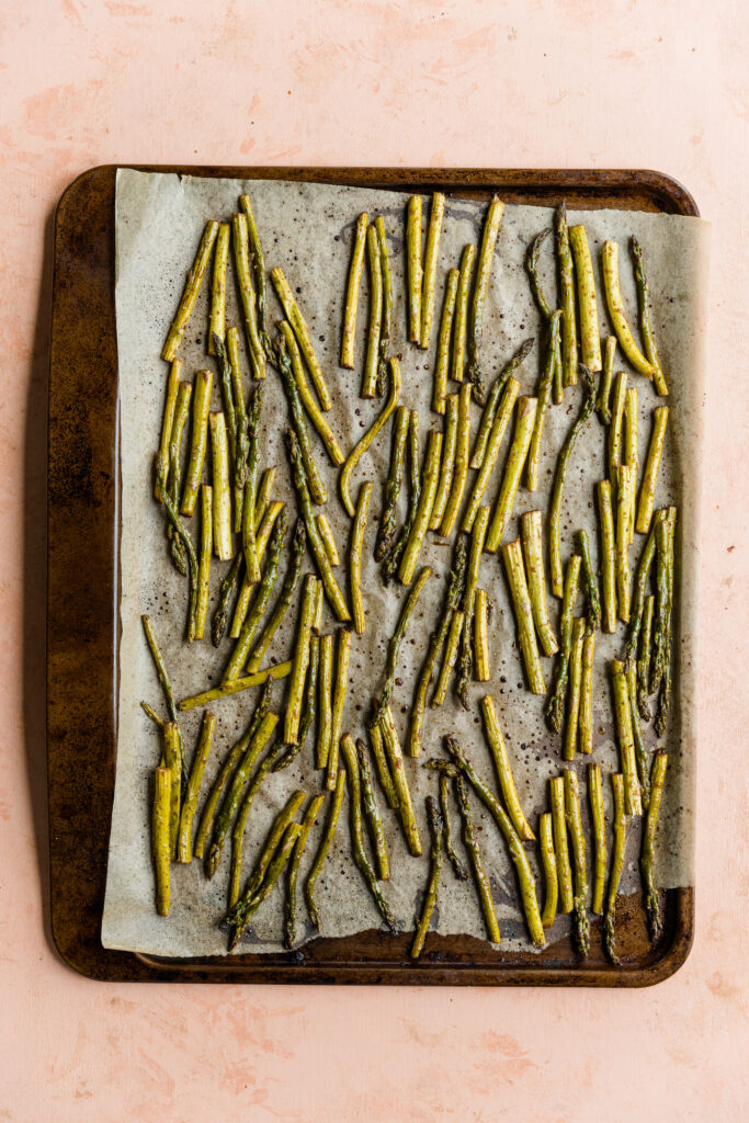 Roasted asparagus on a parchment paper lined baking sheet.
