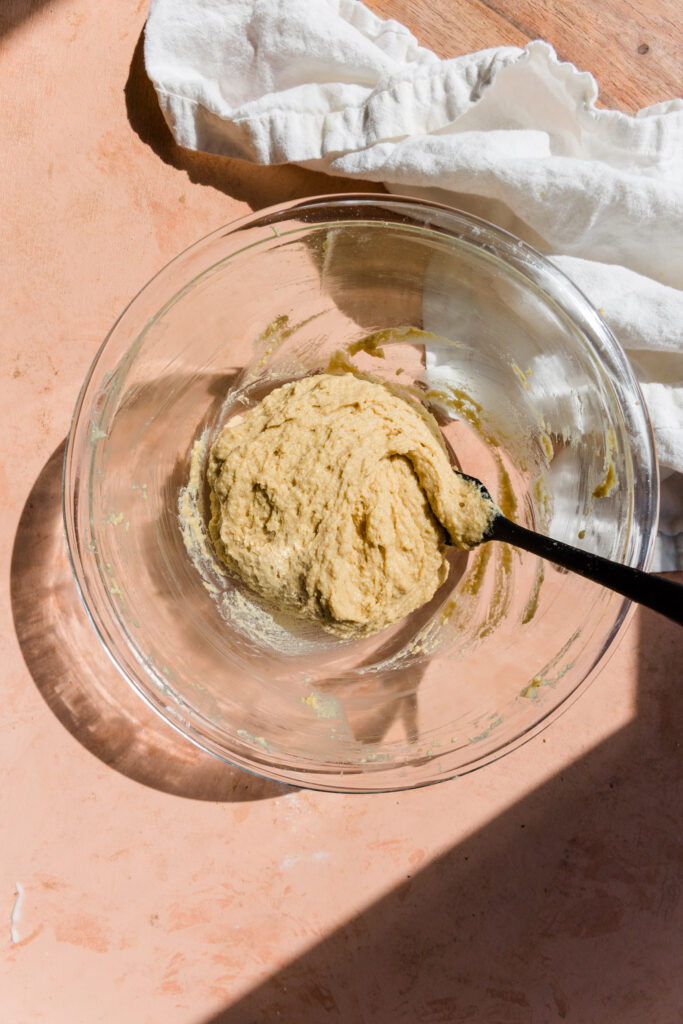Hamburger bun batter in glass mixing bowl with black spatula.