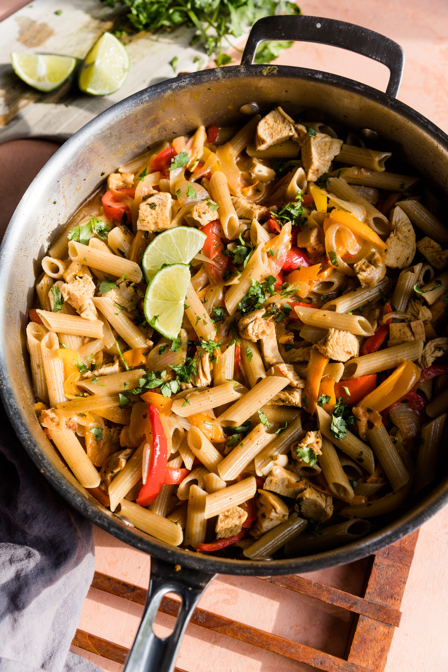 Large pot of fajita chicken pasta with fresh cilantro and lime wedges on the side.