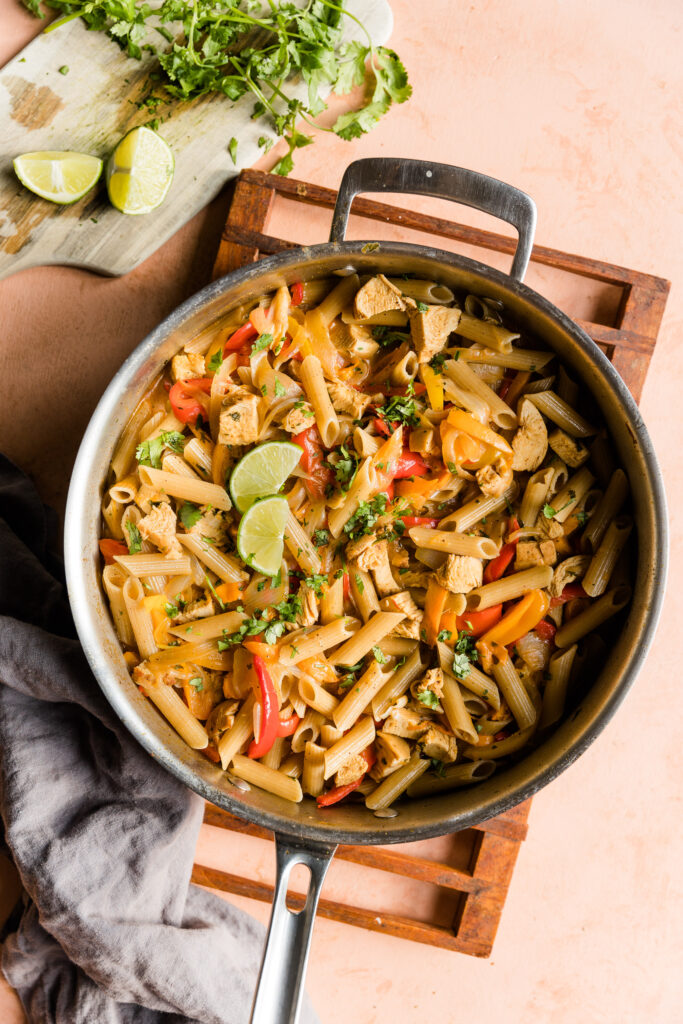 Cooked fajita pasta dinner in pan with lime wedges on top.