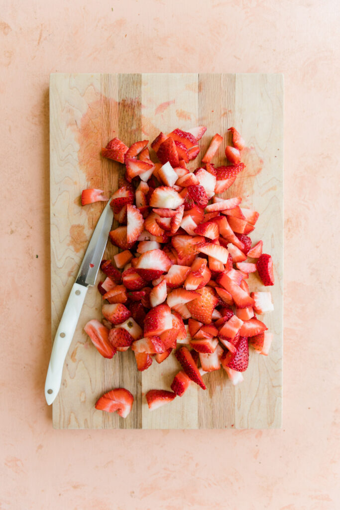 Chopped strawberries on a cutting board with a knife.