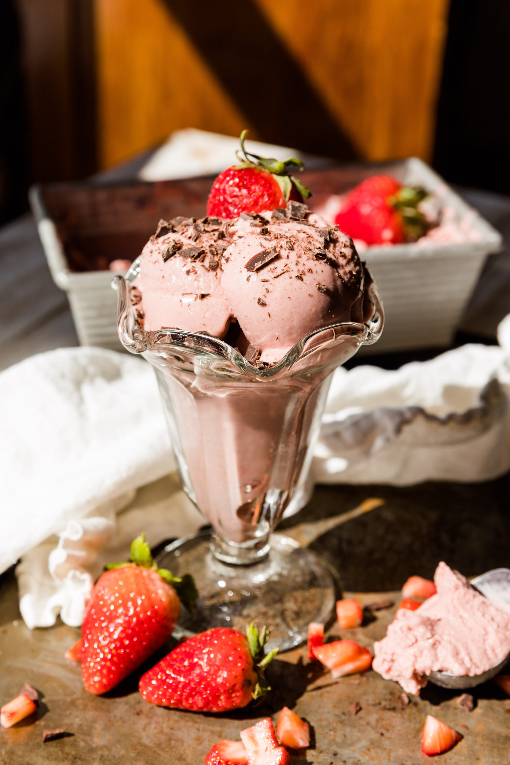 Strawberry ice cream scooped into glass cup with chocolate on top.