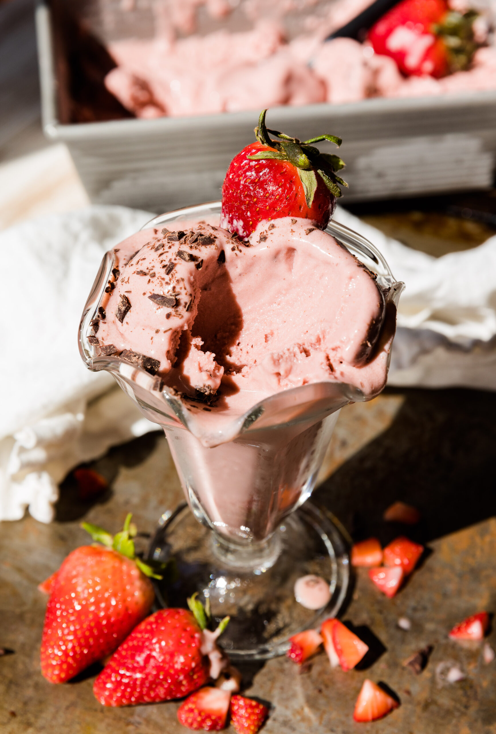 Strawberry ice cream in a scalloped glass cup with fresh strawberries.