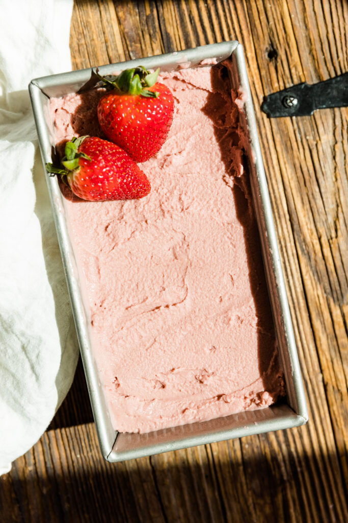Strawberry ice cream in metal bread pan with fresh strawberries on top.