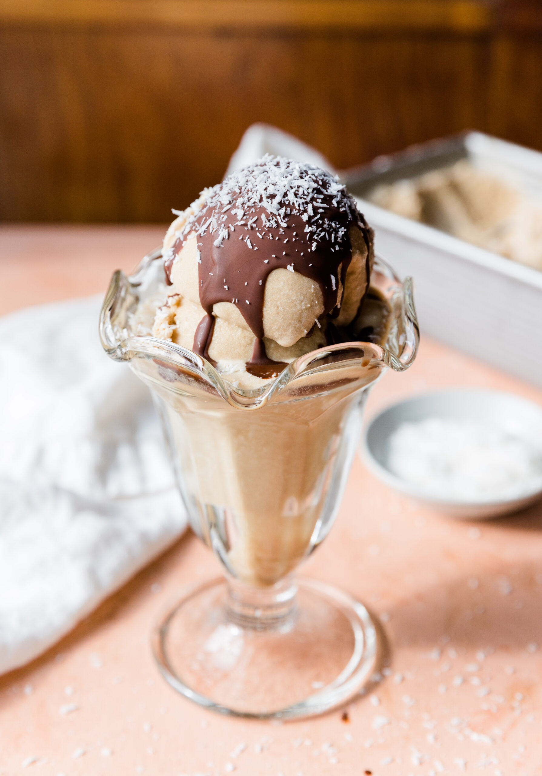Coconut ice cream in glass cup with melted chocolate on top.