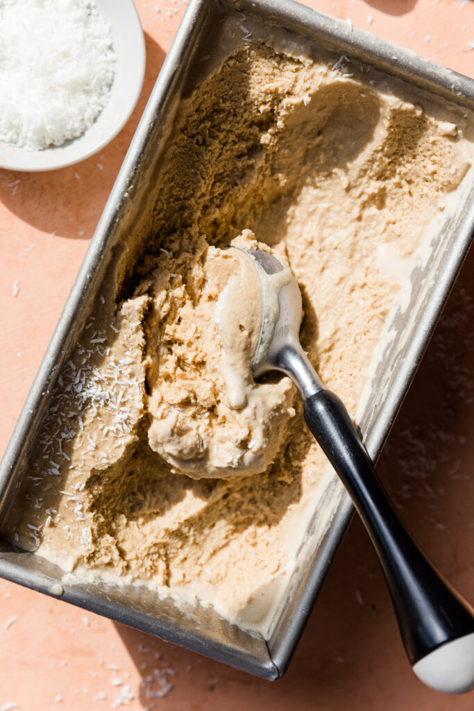 Ice cream scooper in metal loaf pan filled with dairy free coconut ice cream.