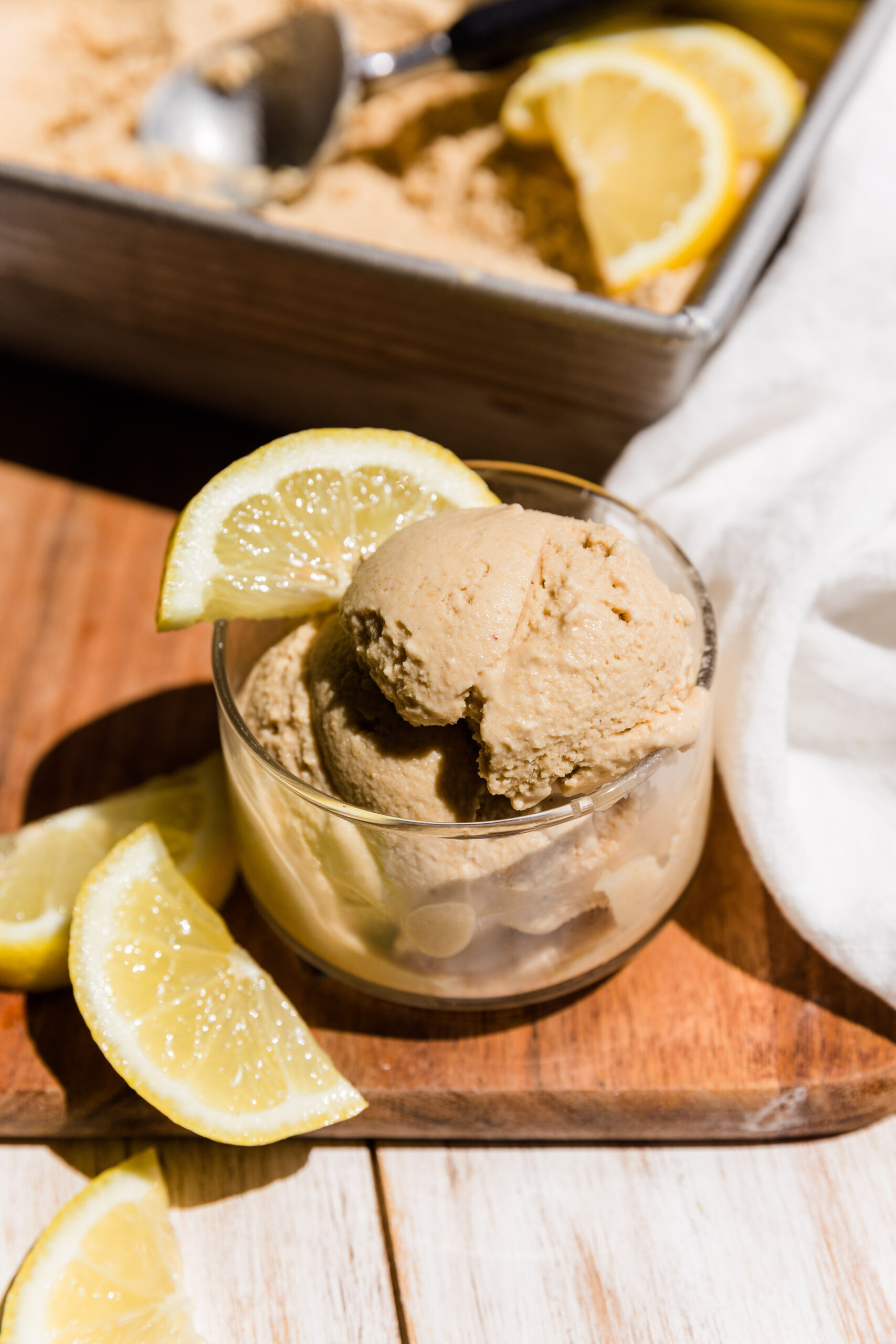 Creamy dairy free lemon ice cream in a small glass bowl with fresh lemon slices.