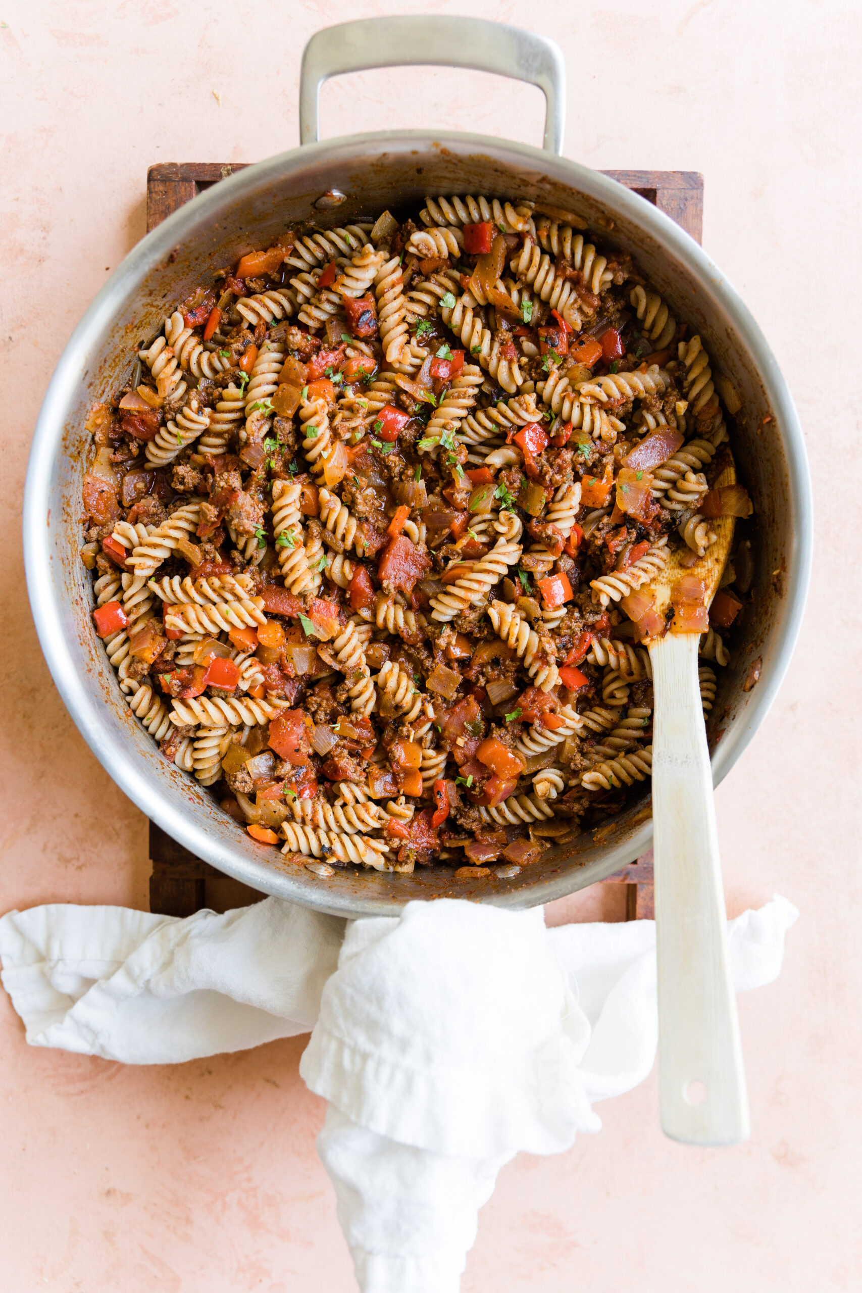 Taco pasta dinner in large pot with white cloth wrapped around the handle and a wooden spoon leaning on the edge.