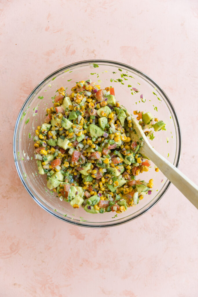 All ingredients for salsa recipe mixed together in glass mixing bowl.