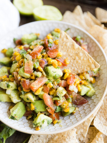 Avocado corn salsa in ceramic bowl with chip scooping some out.