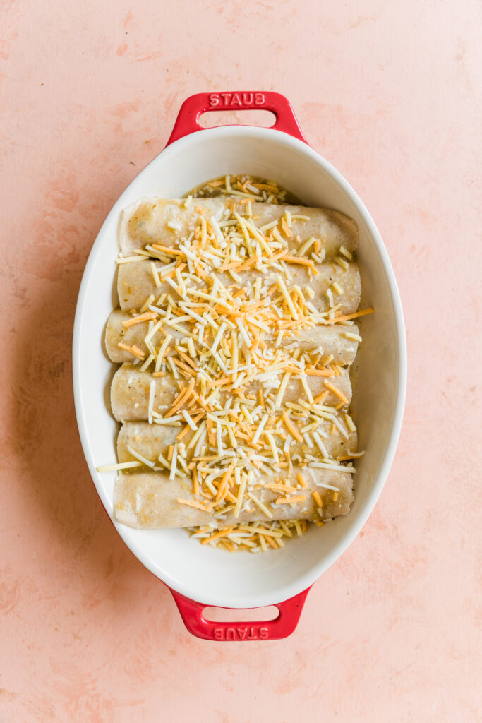 Rolled enchiladas in casserole dish with dairy free shredded cheese on top.