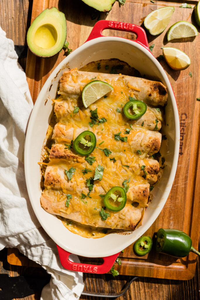 Baked gluten free chicken enchiladas in casserole dish with fresh cilantro, lime, and jalapeno.