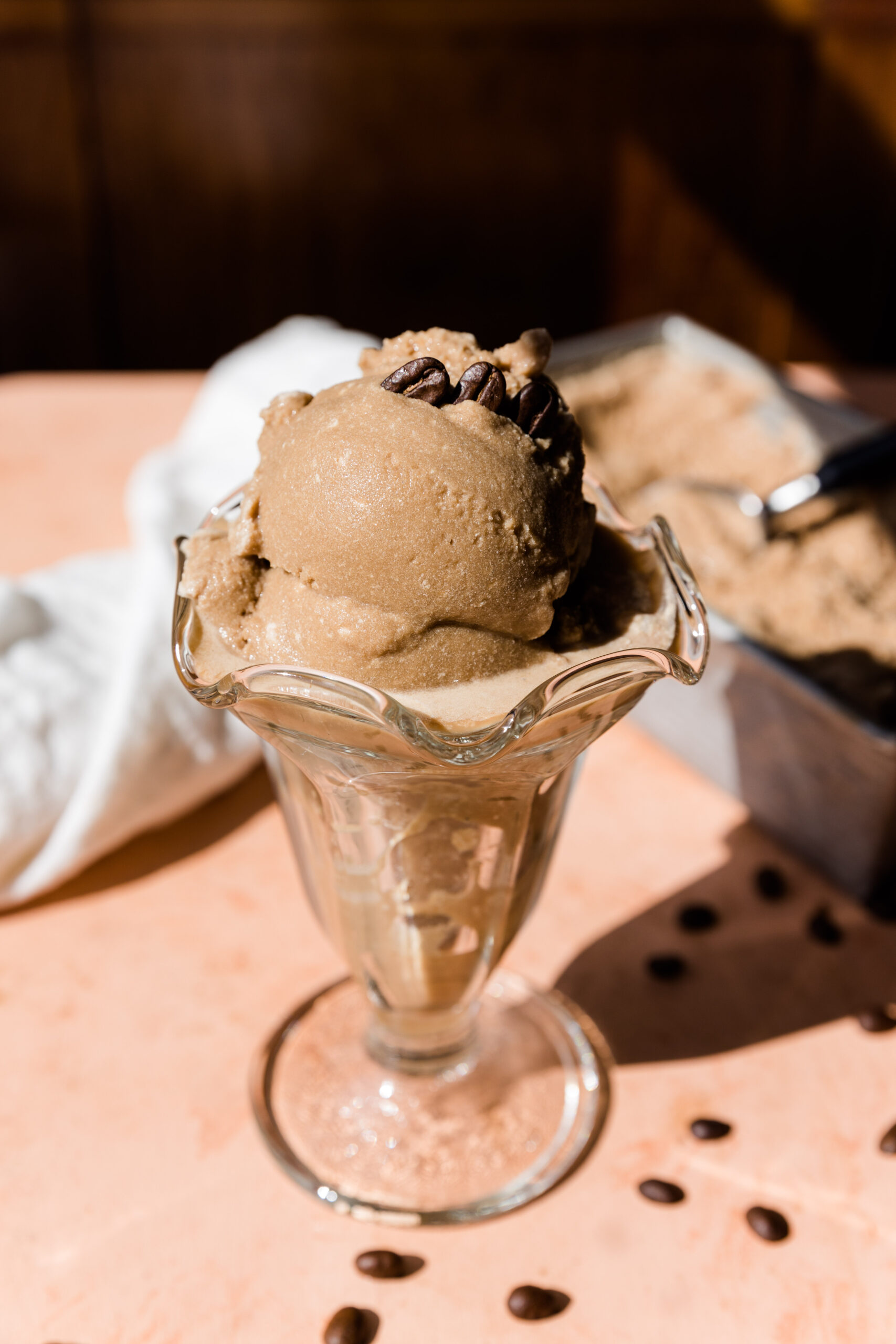 Creamy coffee ice cream in glass ice cream bowl with coffee beans on top.