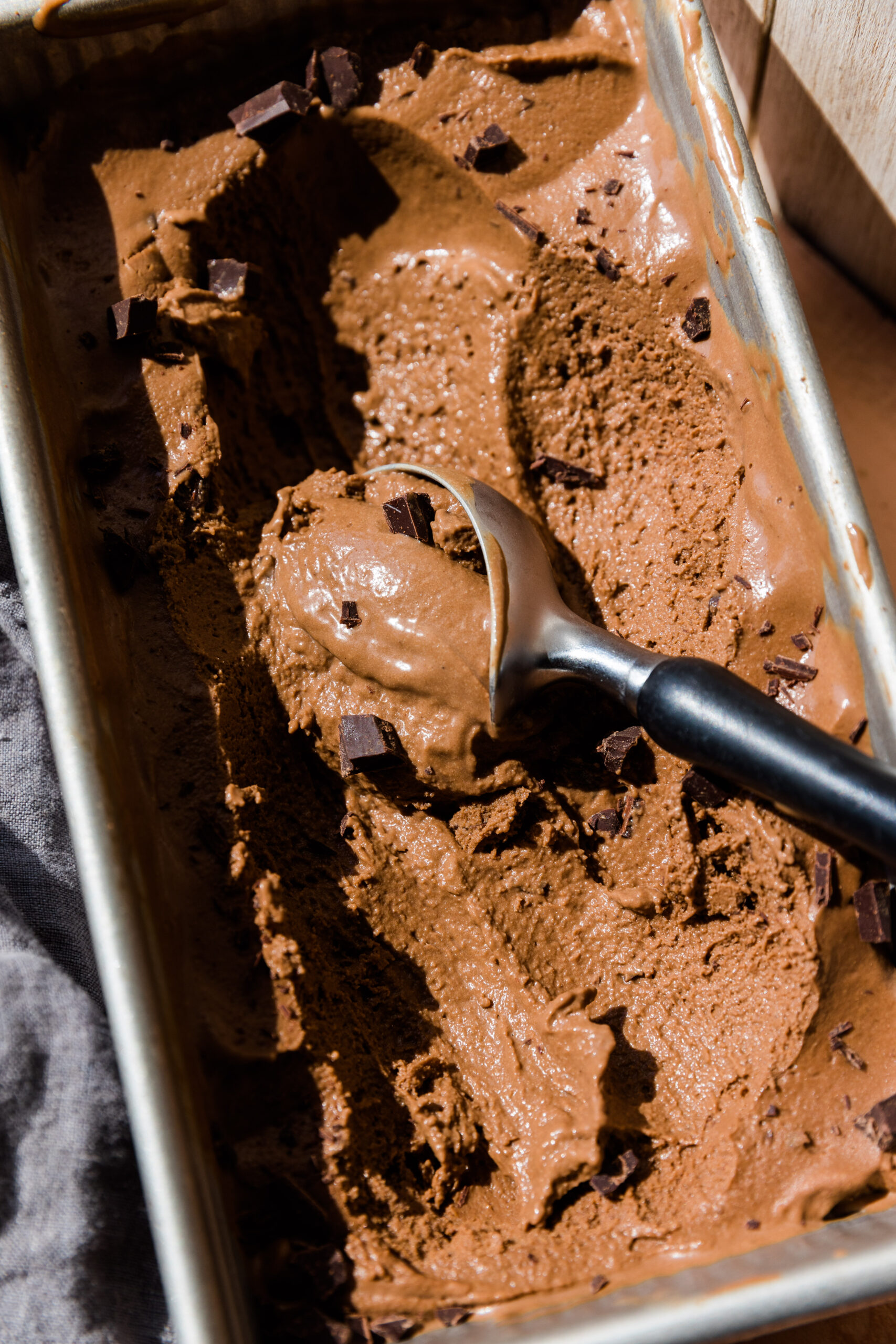 Ice cream scooper scooping out chocolate ice cream with chocolate chunks on top.