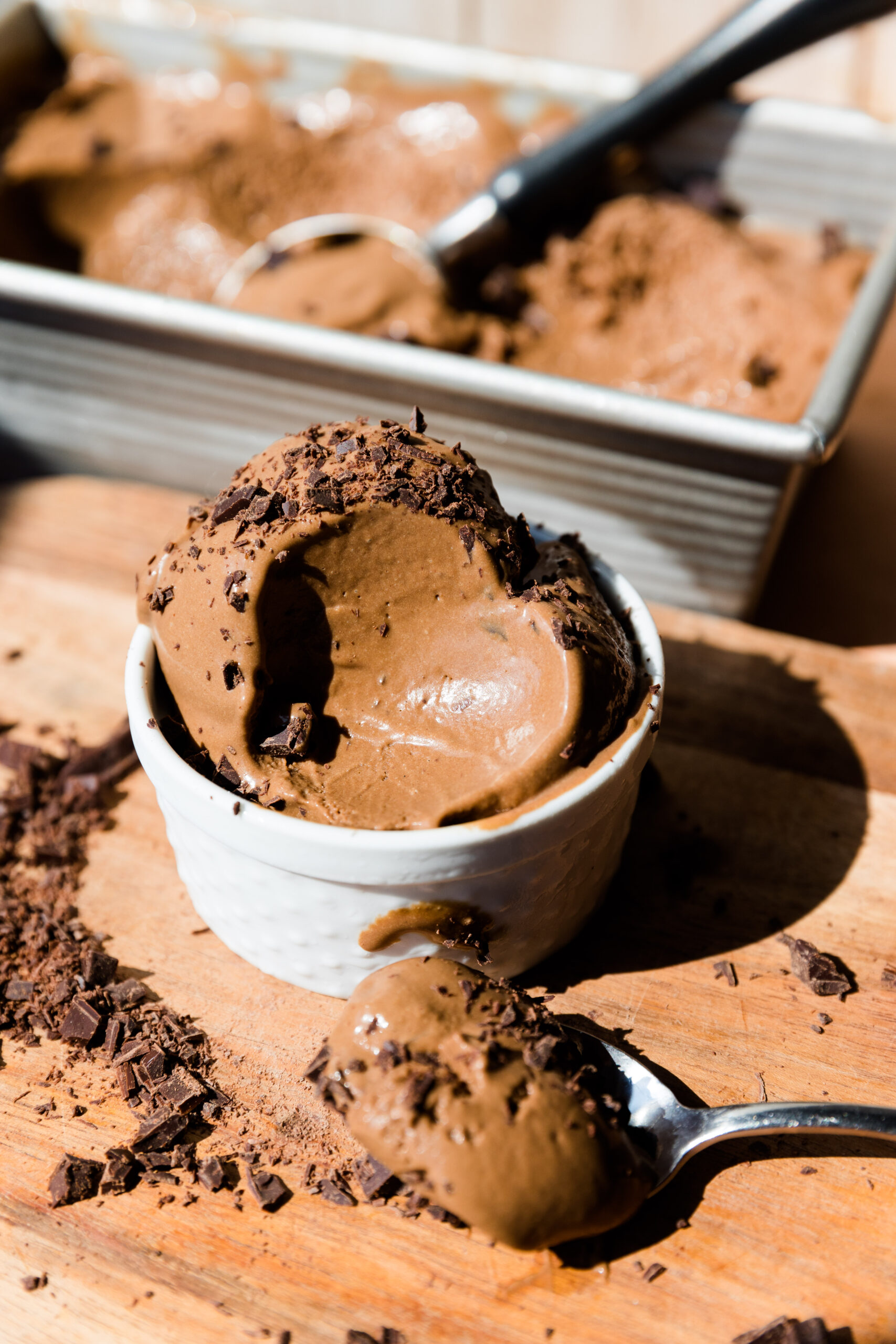 Chocolate ice cream in a white cup with spoon full of ice cream in front.
