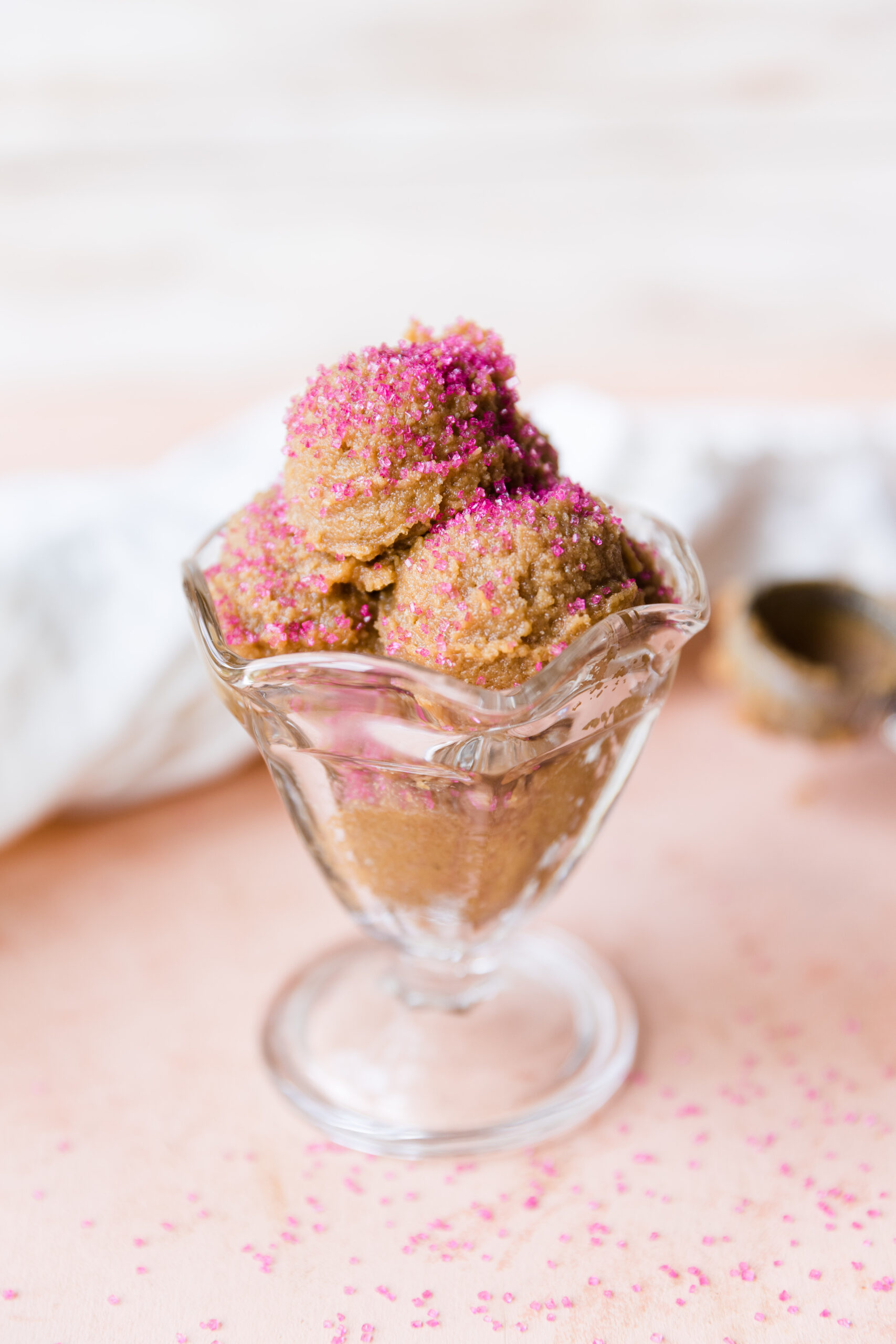 Sugar cookie dough in a glass ice cream bowl with pink sprinkles.