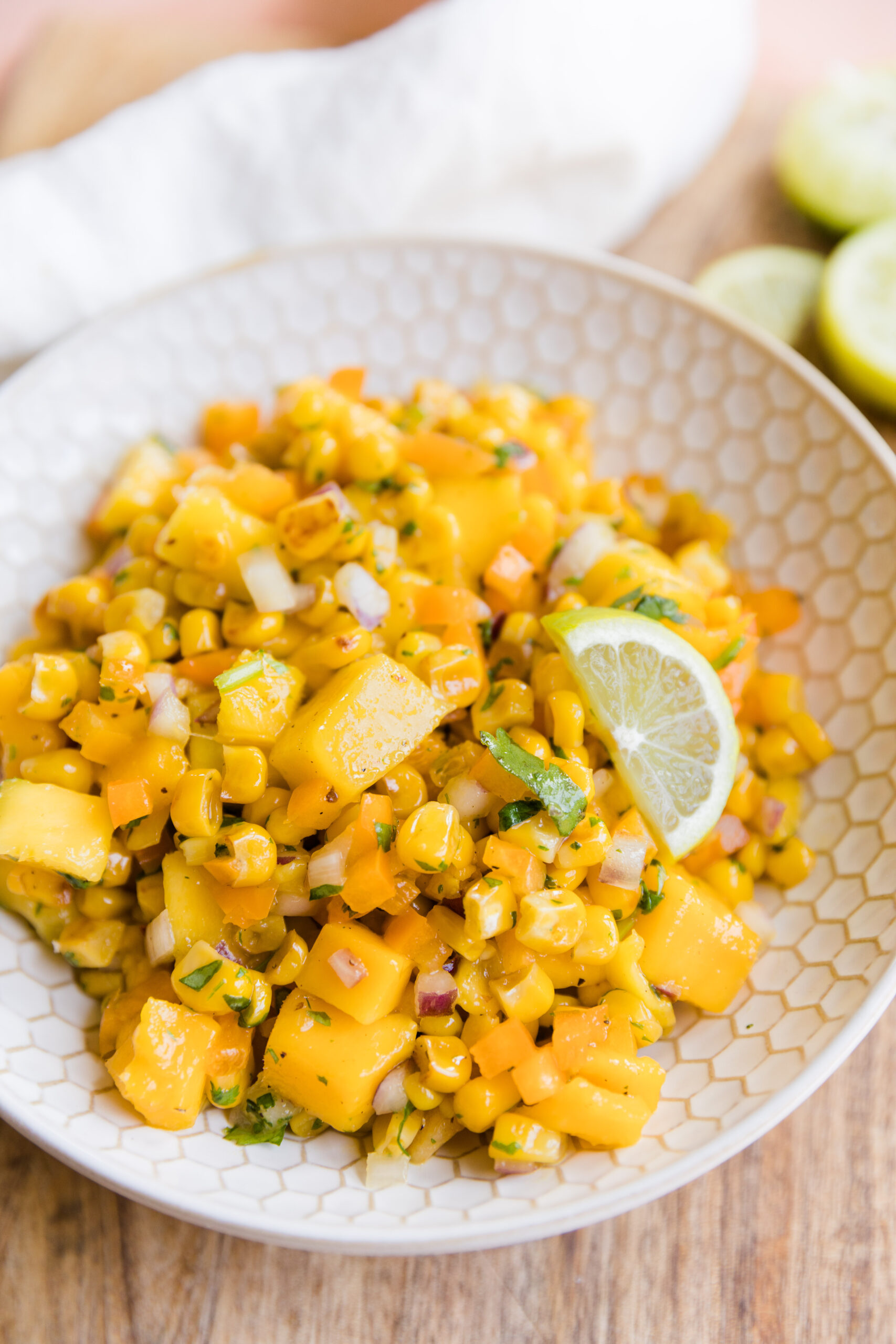 Mango corn salsa in a white ceramic bowl with lime wedge.